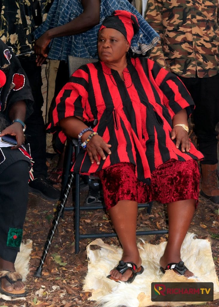 A woman in red and black traditional dress seated outdoors.